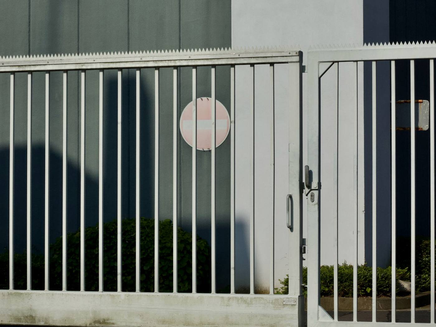 Weißer Metallzaun mit Drehtor vor einem Gewerbegebäude